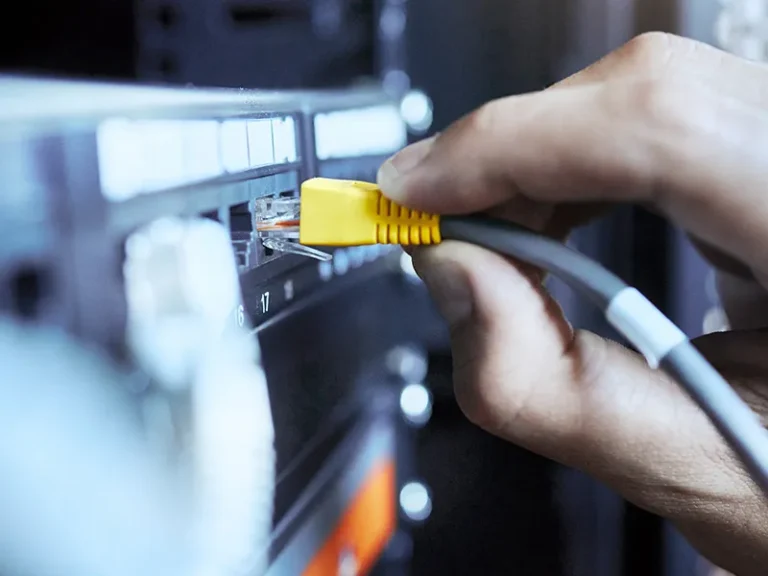 Commercial IT support and maintenance in Western Australia shown through a technician connecting an ethernet cable to a network switch, representing network management, device configuration and integrated electrical, communications and security infrastructure.